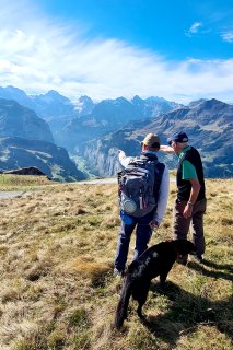 2 Männer und Hund blicken nach Wengen zur Abfahrt.