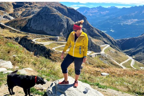 Frau und Hund auf einem Stein mit Tremola Serpetine Straße im Hintergrund.