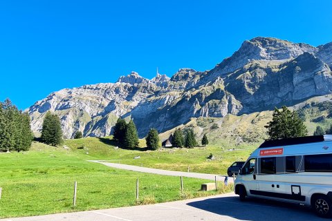 Wohnmobil am Parkplatz während der Fahrt zum Säntis in der Schweiz- Grunes
                           Gras und Berge im Hintergrund.