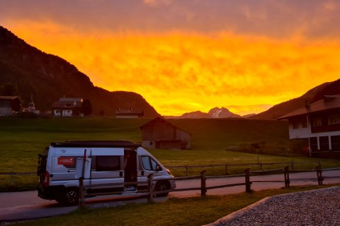 Wohnmobil auf einem Stellplatz in der Schweiz. Der Himmel ist gelb und Orange wegen einen schönen Sonnenuntergang.