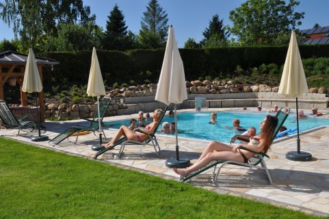 Menschen liegen auf Sonnenliegen am Pool in der Sonne.